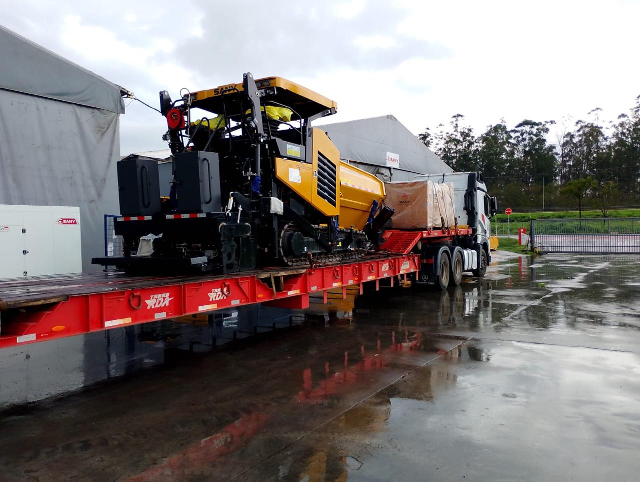 Caminhão RDA transportando máquina pesada em carreta prancha